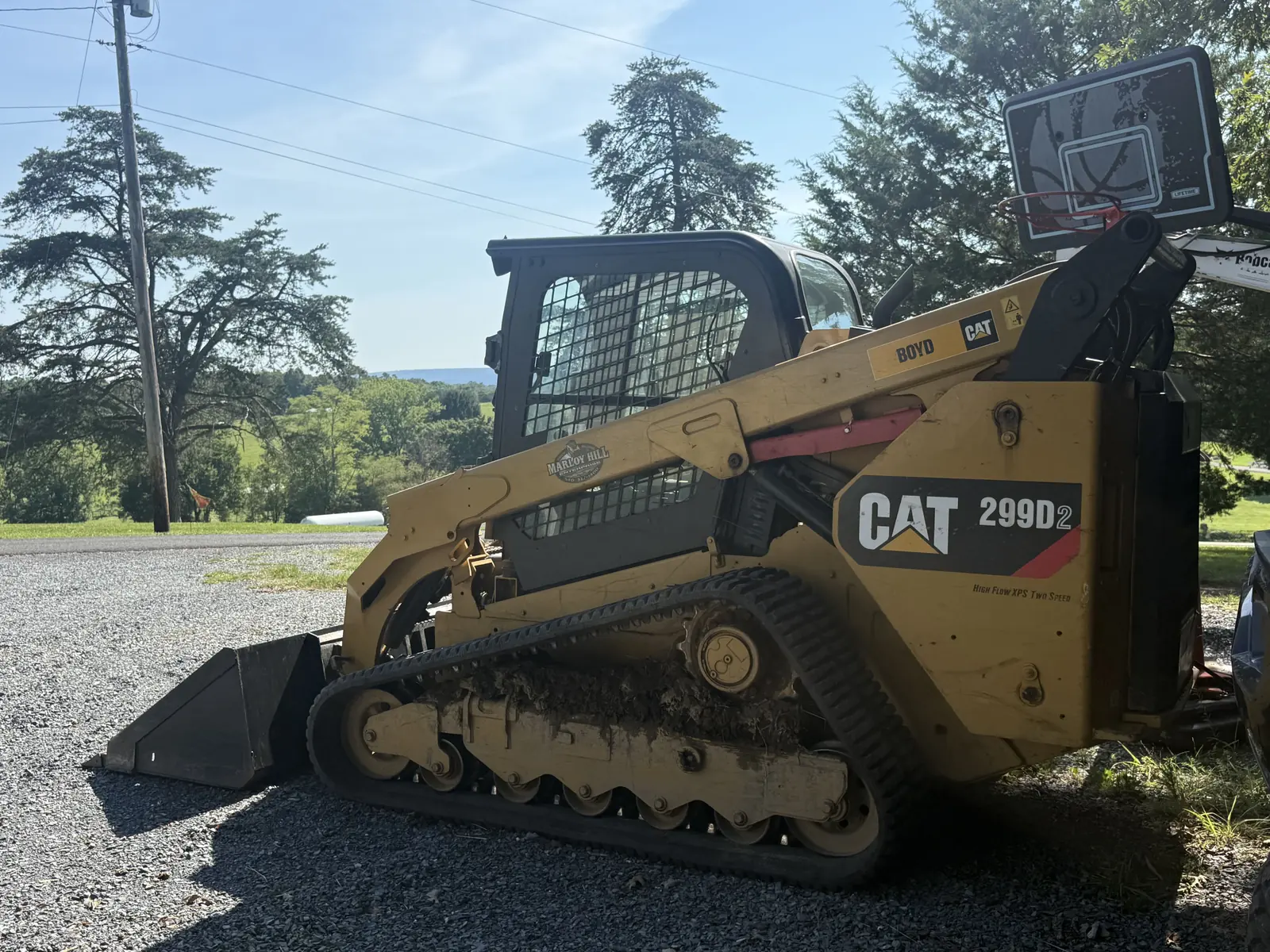 Compact track loader with a bucket parked on gravel, ridges in the distance