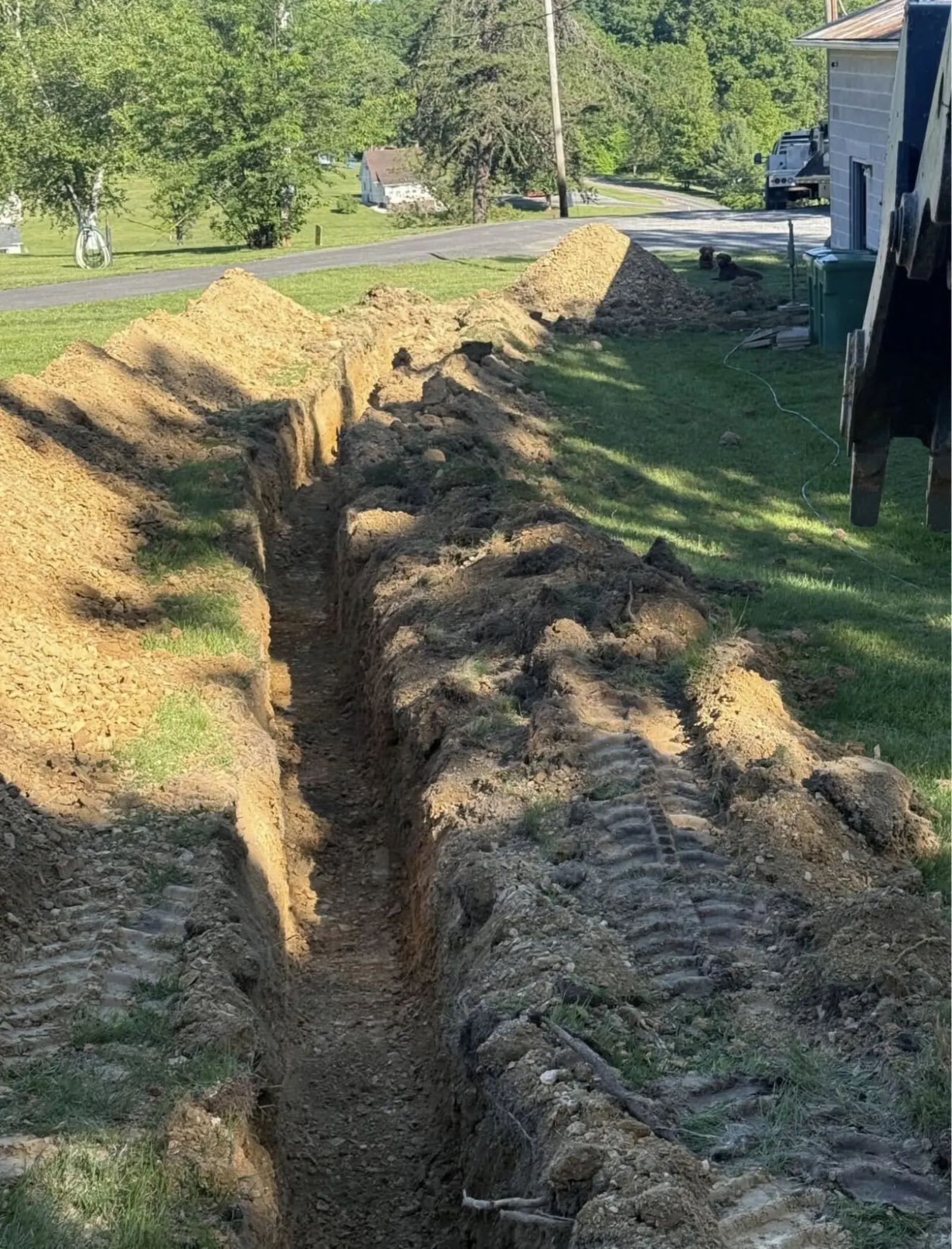 Trench dug across a yard for a drainage line, track marks in the topsoil