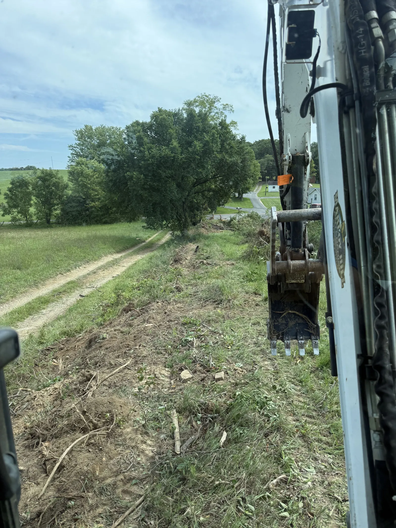 View from the excavator cab while clearing brush along a farm lane