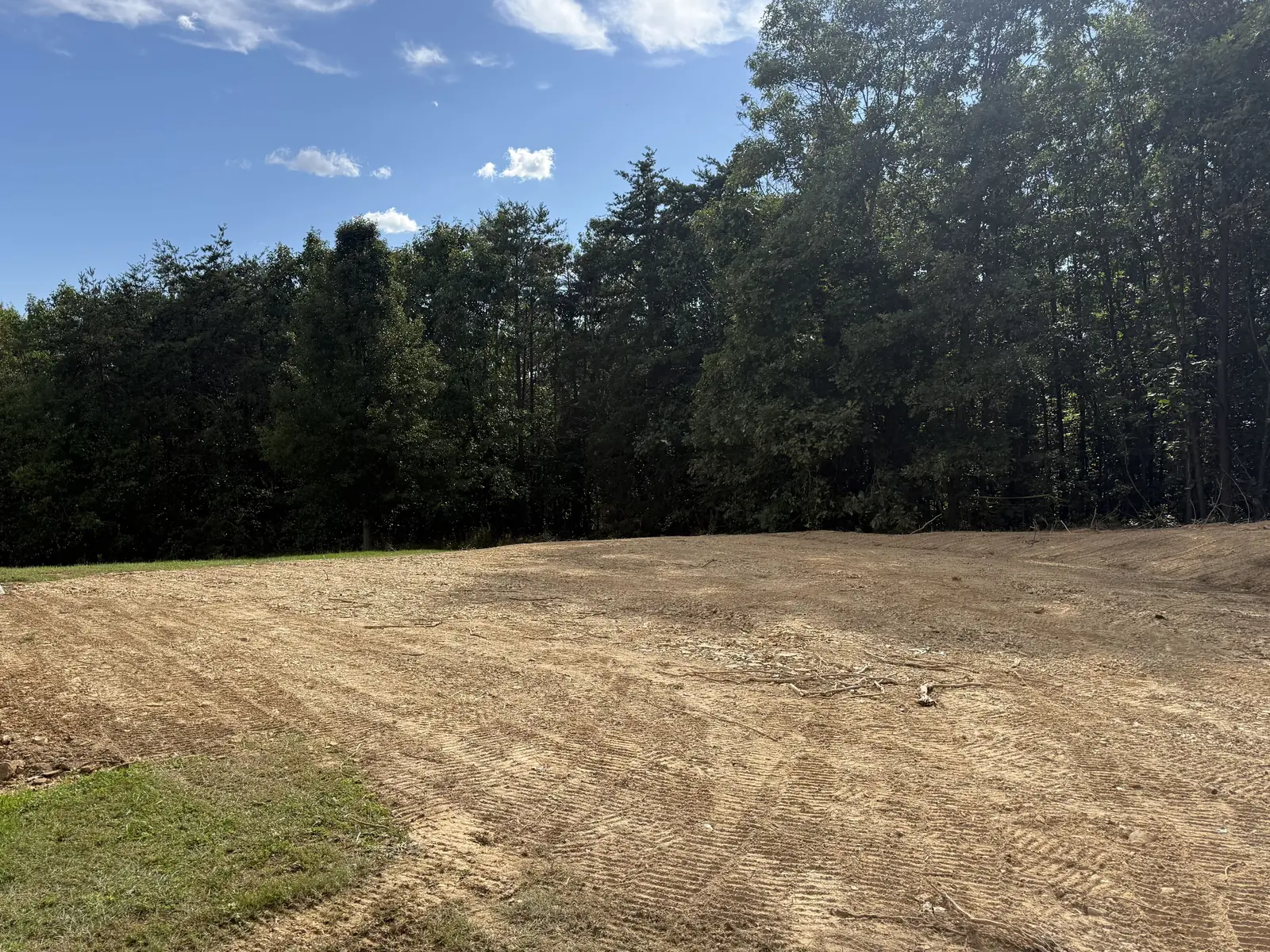 Level graded pad with fresh track marks beside a tree line