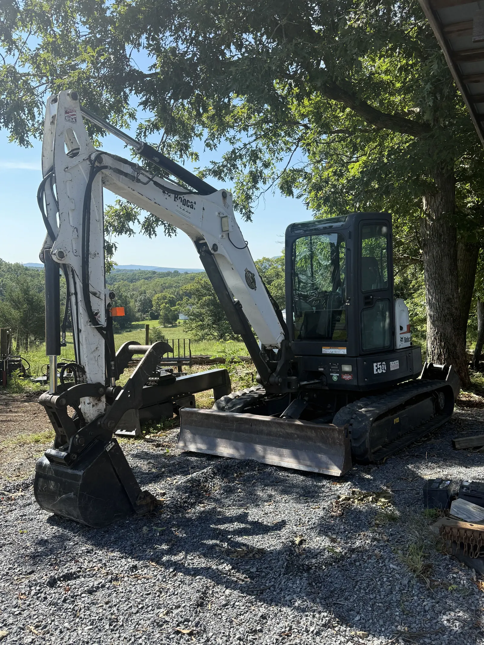 Mini excavator with a digging bucket and blade parked on gravel, valley view behind