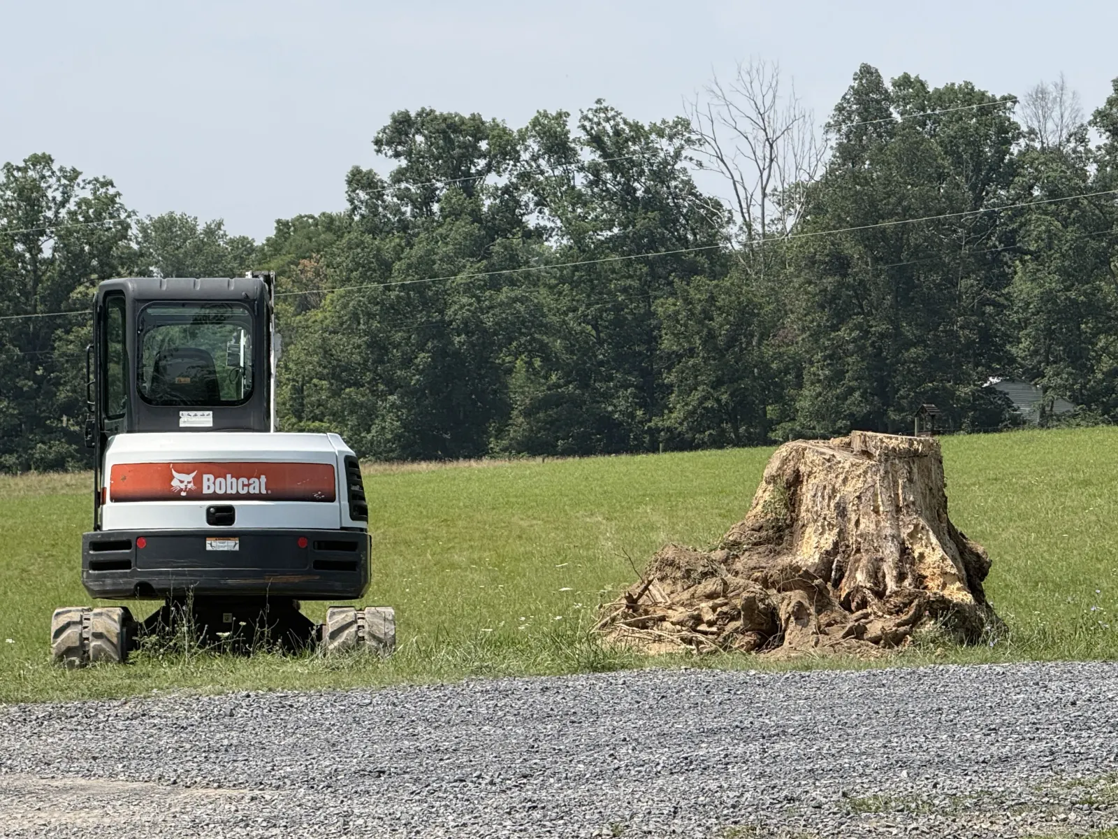 Mini excavator parked beside a large stump in an open field