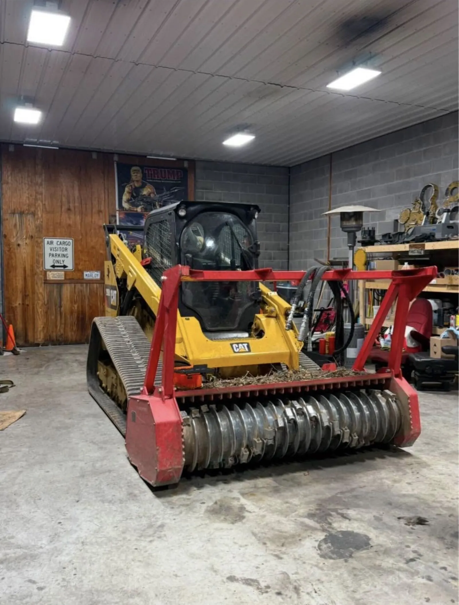 Compact track loader with a forestry mulcher head parked in the shop